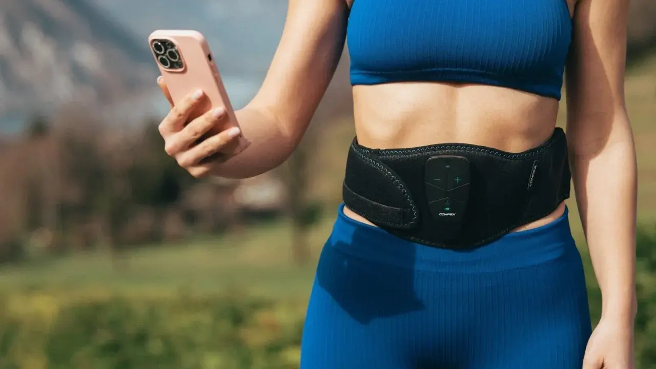 Donna con fascia addominale per tonificare la pancia molle dopo parto, mentre controlla l'app sul suo smartphone.