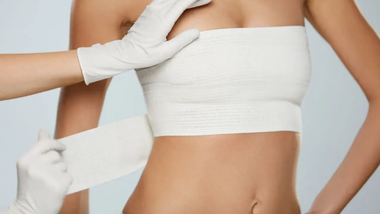 Guida sicura dopo mastoplastica: bendaggio toracico applicato da mani con guanti.