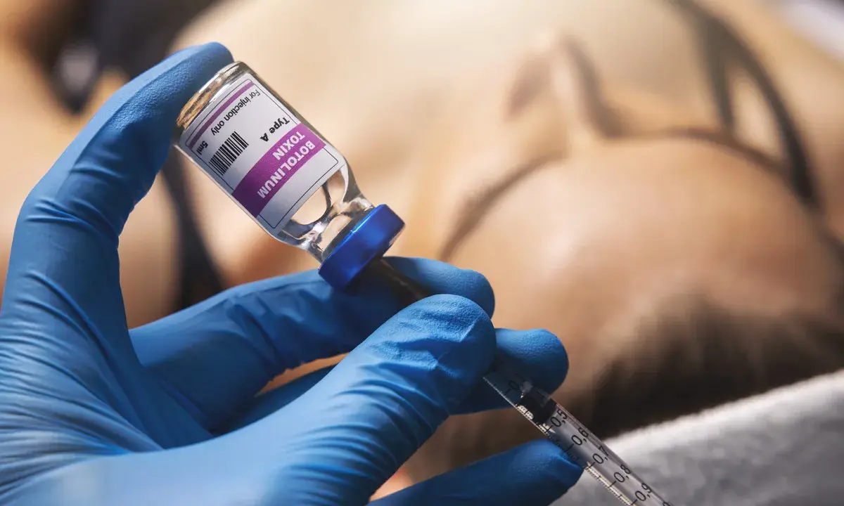 Mano con guanto blu che aspira botulino da fiala. Si valuta il botox mento effetti collaterali.
