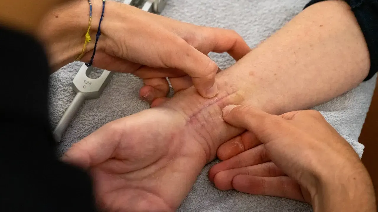 Mani esperte che mostrano come massaggiare una cicatrice sul polso, con un diapason in primo piano.