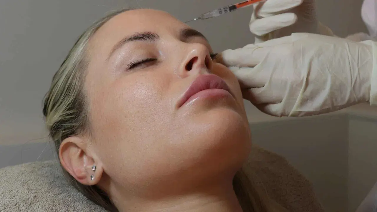Primo piano del **full face viso** di una donna con gli occhi chiusi, mentre una mano guantata le inietta un filler sul naso.