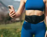 Donna con fascia addominale per tonificare la pancia molle dopo parto, mentre controlla l'app sul suo smartphone.