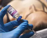 Mano con guanto blu che aspira botulino da fiala. Si valuta il botox mento effetti collaterali.