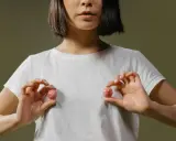 Mani che tengono due sfere rosa, una che ricorda un capezzolo e areola, su una maglietta bianca.