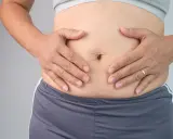 Mani che stringono l'addome, evidenziando la pelle in eccesso e le smagliature.