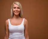 Donna sorridente con capelli biondi, indossa una canottiera bianca. Potrebbe essere una persona che ha deciso di rifarsi il seno a 40 anni per sentirsi più sicura.