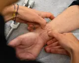 Mani esperte che mostrano come massaggiare una cicatrice sul polso, con un diapason in primo piano.