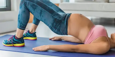 Donna in posa yoga, con i fianchi ad ali di farfalla, solleva il bacino su un tappetino blu.