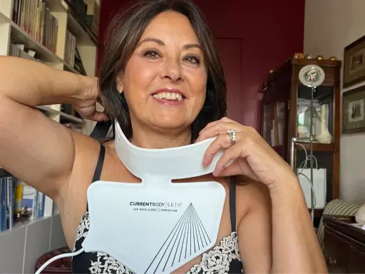 Donna sorridente prova un dispositivo LED per collo e décolleté, una soluzione per le rughe décolleté come eliminarle.