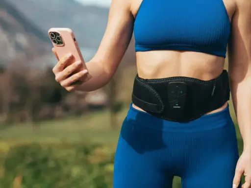 Donna con fascia addominale per tonificare la pancia molle dopo parto, mentre controlla l'app sul suo smartphone.