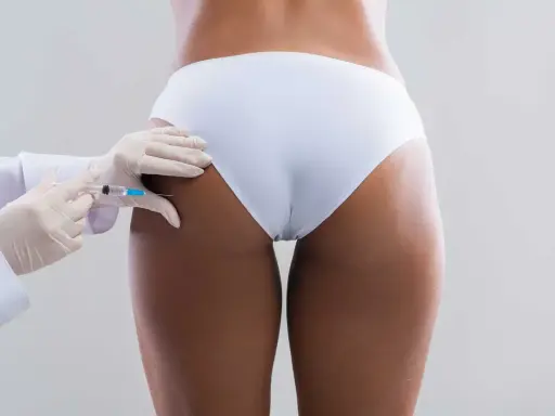 Mani guantate iniettano filler al sedere per un aumento e rimodellamento estetico.