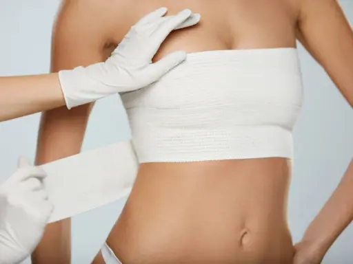 Guida sicura dopo mastoplastica: bendaggio toracico applicato da mani con guanti.