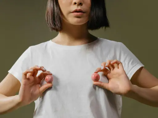 Mani che tengono due sfere rosa, una che ricorda un capezzolo e areola, su una maglietta bianca.