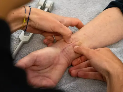 Mani esperte che mostrano come massaggiare una cicatrice sul polso, con un diapason in primo piano.