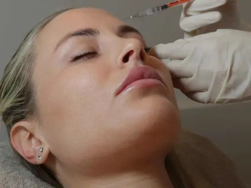 Primo piano del **full face viso** di una donna con gli occhi chiusi, mentre una mano guantata le inietta un filler sul naso.