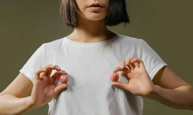Mani che tengono due sfere rosa, una che ricorda un capezzolo e areola, su una maglietta bianca.