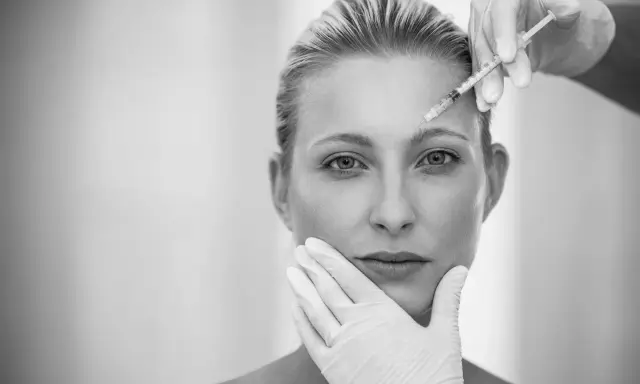 Ritocchino per combattere i segni del tempo e del sole. Botox sulla fronte, mani guantate che accarezzano il viso.