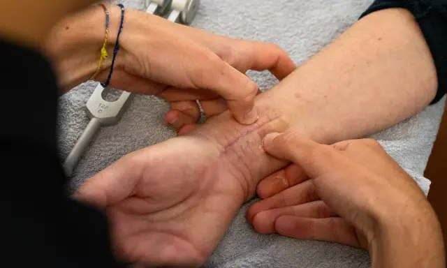 Mani esperte che mostrano come massaggiare una cicatrice sul polso, con un diapason in primo piano.