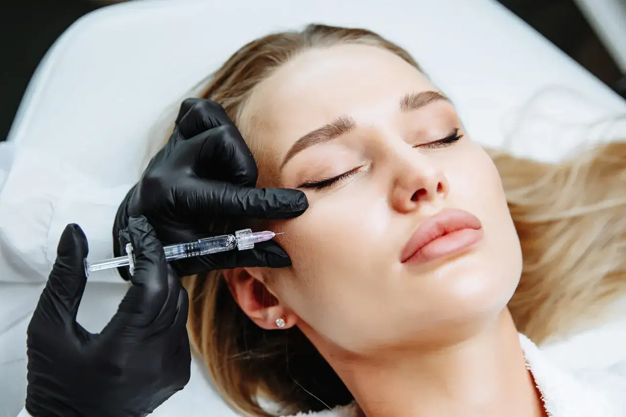Mano con guanto nero inietta una fiala sul viso di una donna. Trattamento di medicina estetica con esosomi viso per un aspetto pi&ugrave; giovane.