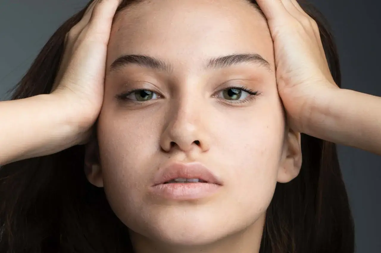 Primo piano di una giovane donna con mani tra i capelli, che evidenzia l'elasticità della pelle e uno sguardo intenso.